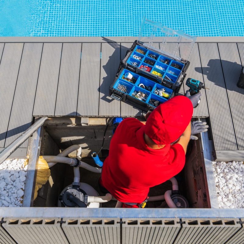 Professional Technician in Red Uniform Performing Regular Pool Maintenance Procedures. Open Toolbox with Different Tools and Components in Front of Him. Top View.
